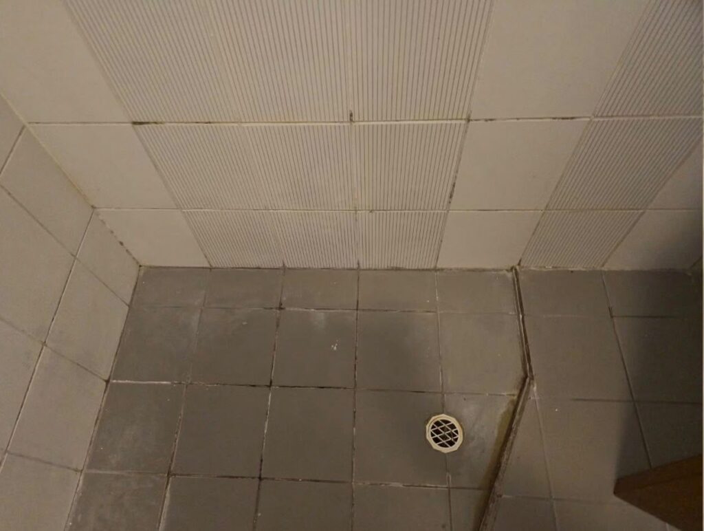 Shower recess before restoration, with stained grout and perished silicone in the corners