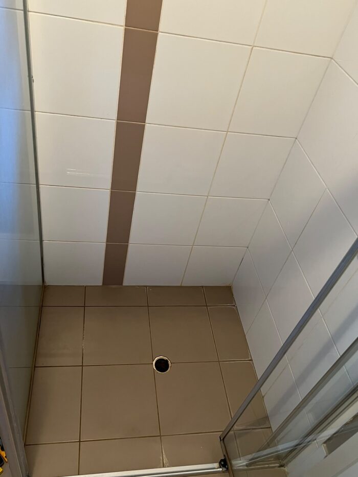 Shower base before repair, with crumbling grout and gaps opening around the perimeter